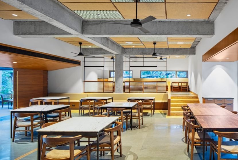 Architecture studio Hundredhands designed Bangalore International Centre in India. A cavernous auditorium lined with angled, perforated wooden panels sits at the heart of the cultural centre. The CAFE is casual and warm with Windmill ASANA model in Matt Black adorning the ceiling