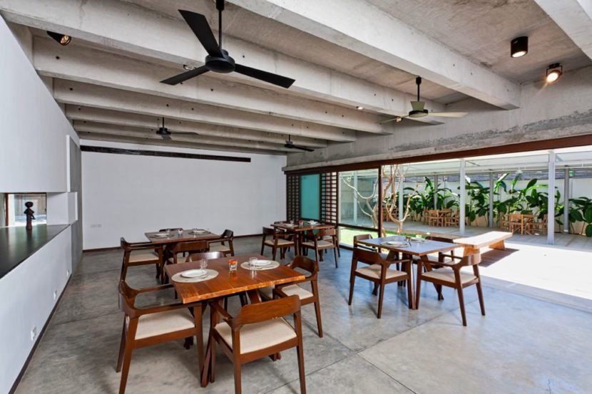 Modern restaurant with large open space water bodies with neutral concrete and wood decor with Modern Windmill fan ASANA model in Matt Black finish